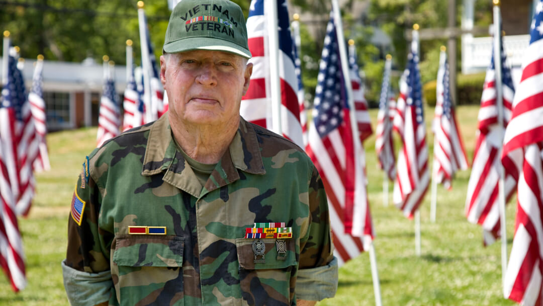 Vietnam Veteran standing in front of rows of American Flags