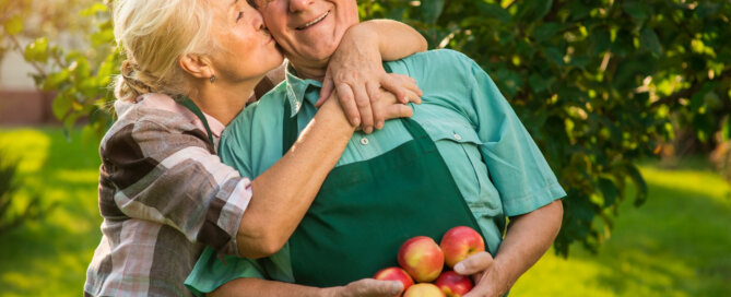 wife kissing her husband under an apple tree he is holding apples and wearing an apron